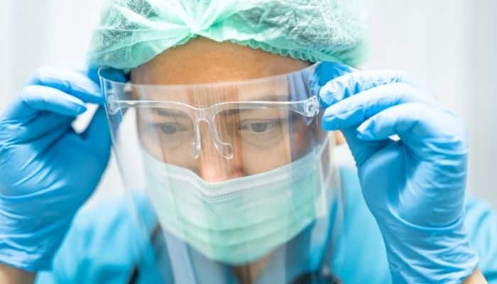 A medical professional wearing protective gloves, hair cover, face mask and face shield