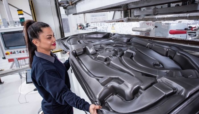 A woman removing a large black plastic thermoformed plastic part from the machine