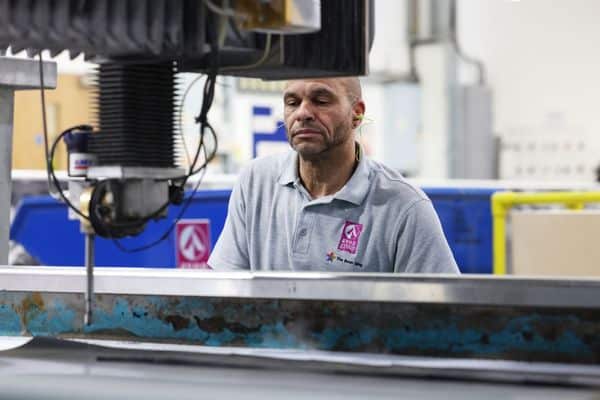A operator watches a waterjet cutting machine in operation at the AGM Bristol factory