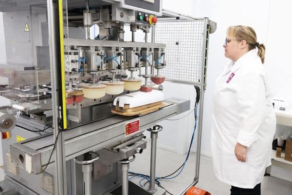 A full colour pad printing machine printing onto a white plastic moulded housing, overseen by a female operative wearing a white coat