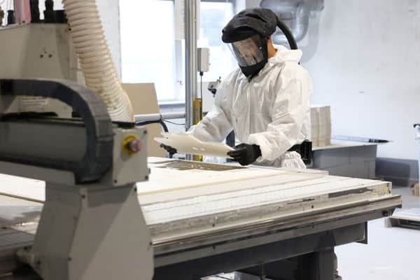 A CNC routing machine operated by a man in a respiration suit cutting high temperature insulation board