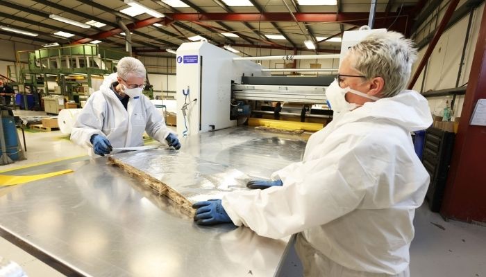 Two operatives dressed in white PPE removing a section of foil laminated mineral insulation fleece from a machine at Avon TSA.